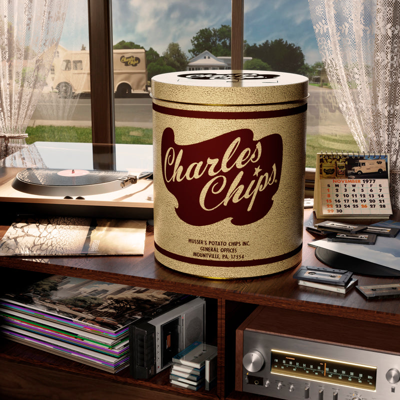 Vintage Charles Chips tin placed on a windowsill inside a cozy home, with a classic Charles Chips delivery truck parked outside. The scene is nostalgically decorated with a phonograph and vinyl records, evoking the timeless charm of the brand's heritage