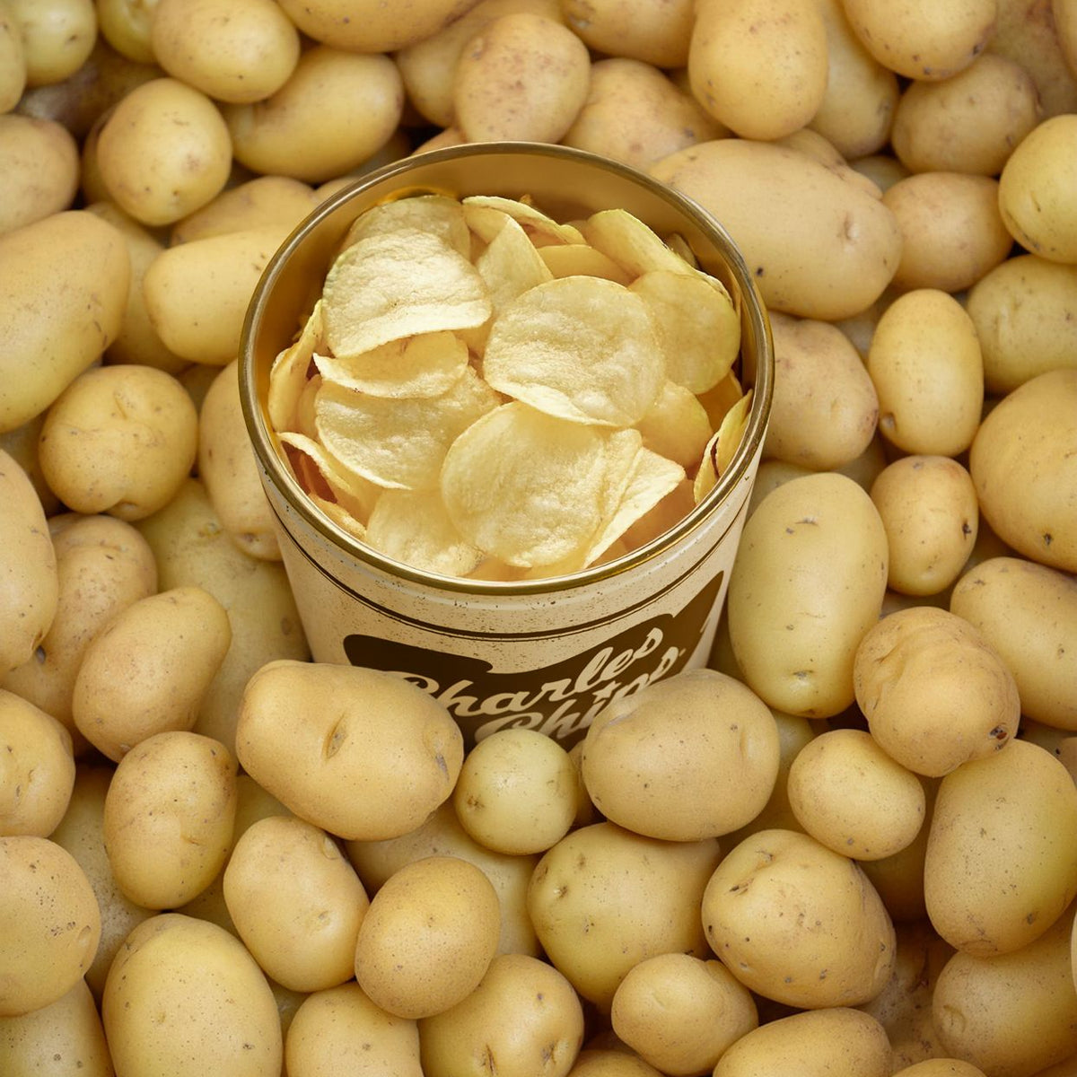 Can of potato chips surrounded by raw potatoes